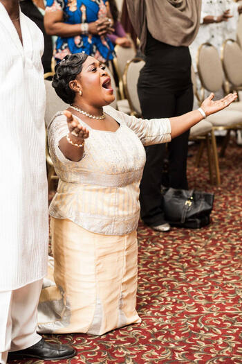 Photograph of mother giving praise during a baby dedication at a Ghanaian church.